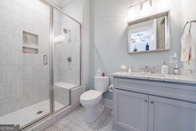 bathroom featuring ceiling fan, toilet, a shower with shower door, and vanity