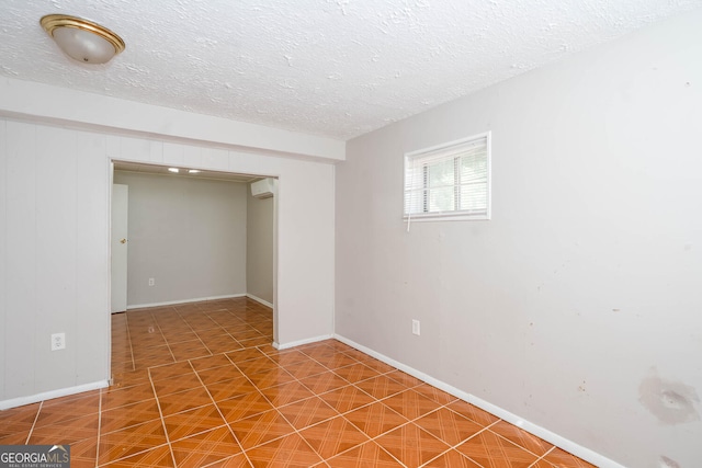 tiled empty room with a wall unit AC, a textured ceiling, and baseboards