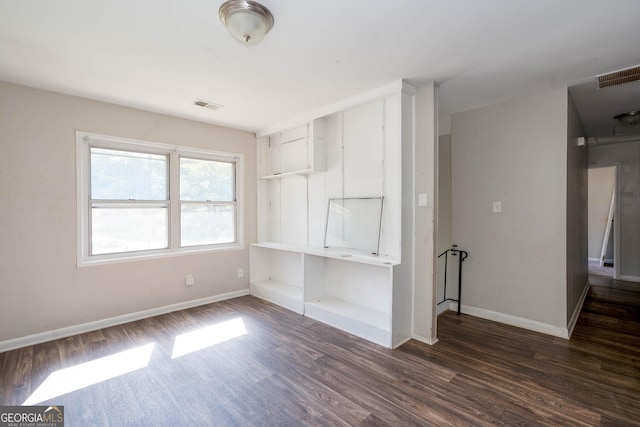 empty room with dark wood-style floors, visible vents, and baseboards