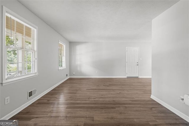 spare room with dark wood-style floors, visible vents, a textured ceiling, and baseboards