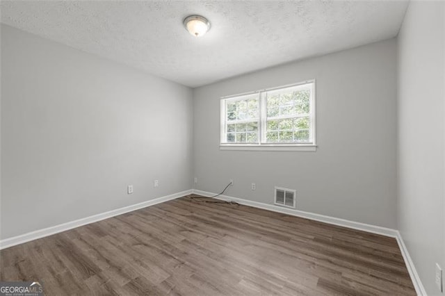 unfurnished room with a textured ceiling, wood finished floors, visible vents, and baseboards