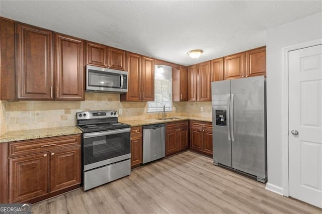 kitchen featuring light stone countertops, a sink, stainless steel appliances, light wood-style floors, and backsplash