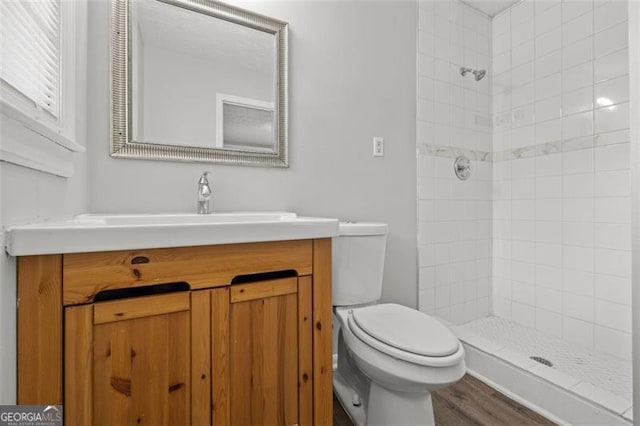 bathroom featuring vanity, toilet, wood finished floors, and tiled shower