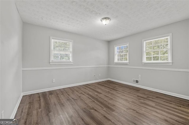 empty room featuring visible vents, a textured ceiling, baseboards, and wood finished floors