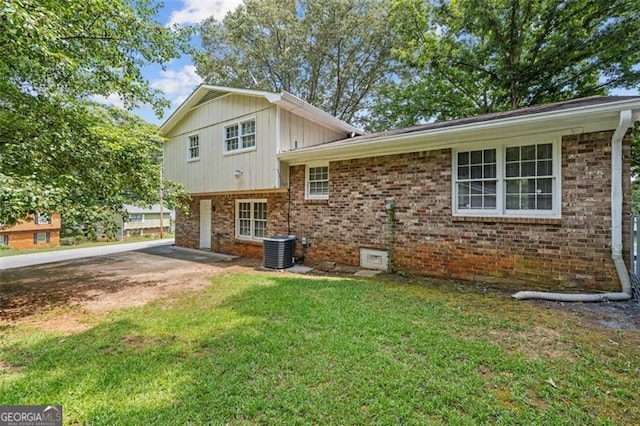 split level home with a front lawn, central AC unit, and brick siding