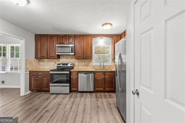 kitchen featuring light wood finished floors, a sink, stainless steel appliances, a textured ceiling, and backsplash