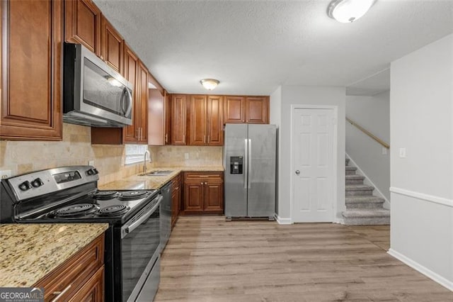 kitchen with a sink, a textured ceiling, light wood-style floors, appliances with stainless steel finishes, and decorative backsplash