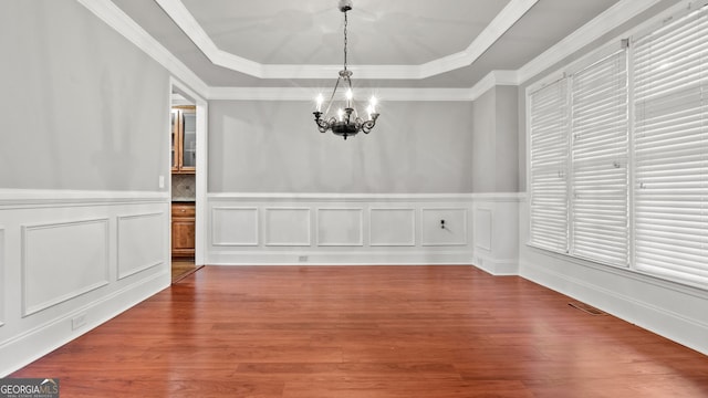 unfurnished dining area with hardwood / wood-style floors, a chandelier, crown molding, and a tray ceiling