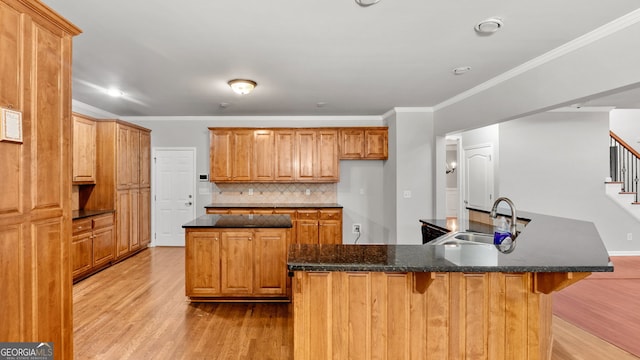 kitchen with backsplash, a center island with sink, ornamental molding, and sink