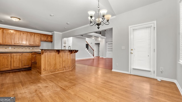 kitchen featuring pendant lighting, decorative backsplash, light wood-type flooring, a notable chandelier, and a breakfast bar area