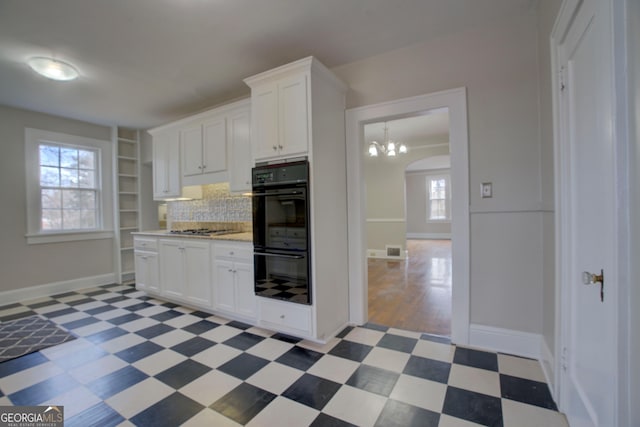 kitchen featuring stainless steel gas cooktop, white cabinetry, a chandelier, double oven, and backsplash