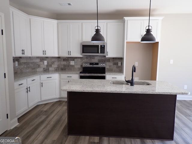 kitchen with appliances with stainless steel finishes, wood-type flooring, an island with sink, hanging light fixtures, and white cabinets