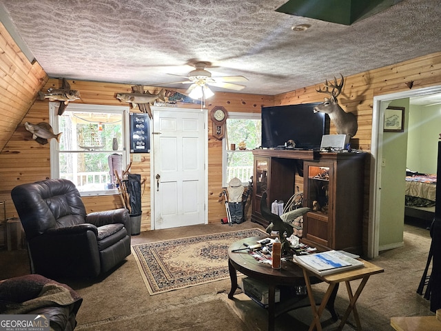 carpeted living room with ceiling fan, wooden walls, and a textured ceiling