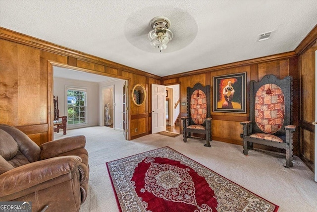 sitting room featuring a ceiling fan, visible vents, wood walls, ornamental molding, and carpet floors