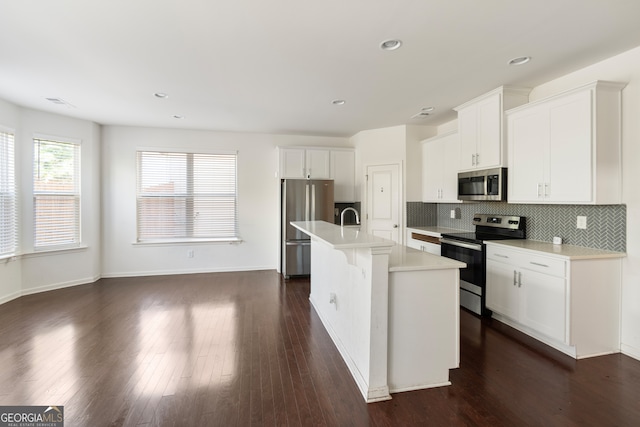 kitchen with appliances with stainless steel finishes, decorative backsplash, white cabinets, dark hardwood / wood-style flooring, and a center island with sink