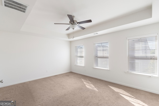 empty room with a tray ceiling, ceiling fan, and carpet flooring