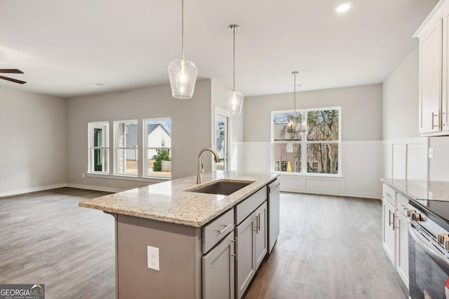 kitchen featuring a center island with sink, sink, decorative light fixtures, light stone counters, and stainless steel appliances