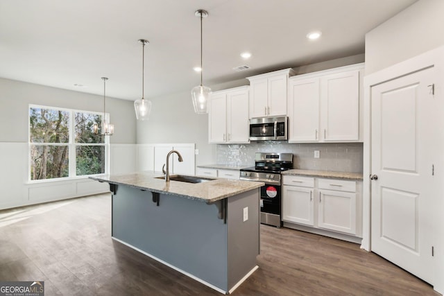 kitchen with white cabinets, appliances with stainless steel finishes, a kitchen island with sink, and sink