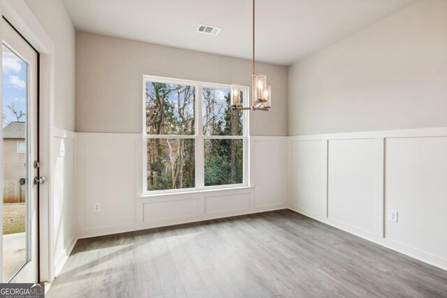 unfurnished dining area with plenty of natural light, wood-type flooring, and an inviting chandelier