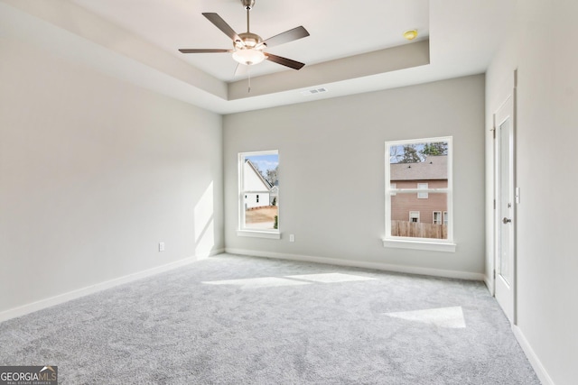 carpeted spare room featuring a tray ceiling and ceiling fan