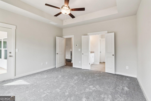 unfurnished bedroom featuring ceiling fan, a raised ceiling, and light carpet