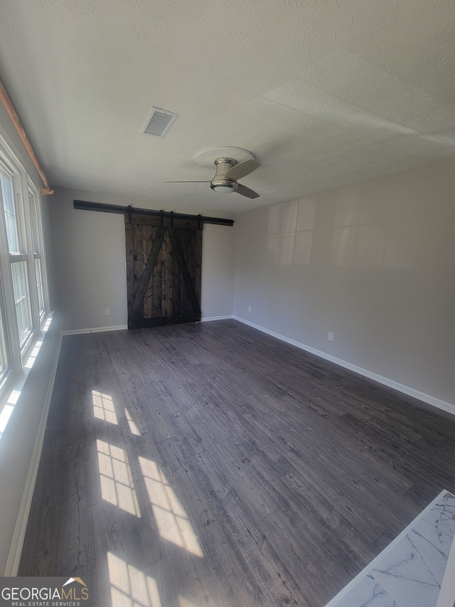 interior space with ceiling fan, a barn door, dark wood-type flooring, and a textured ceiling