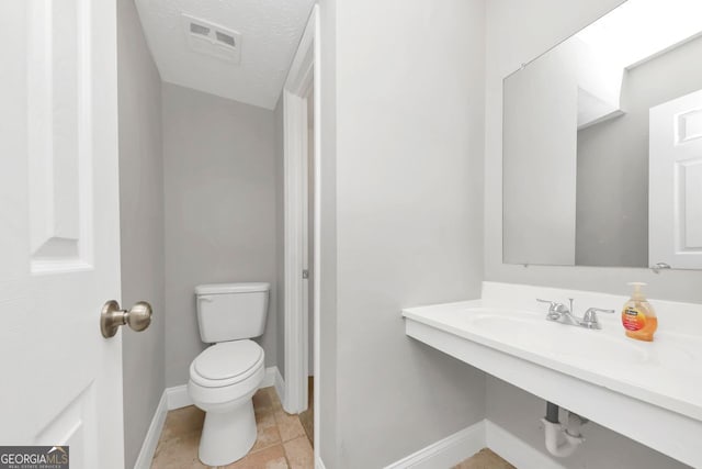 bathroom featuring a textured ceiling, toilet, sink, and tile patterned floors