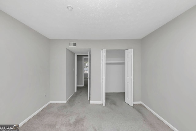 unfurnished bedroom with light colored carpet, a closet, and a textured ceiling