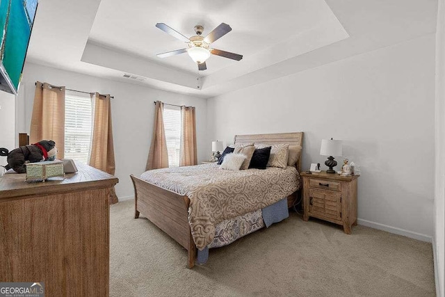 bedroom featuring light carpet, visible vents, baseboards, and a raised ceiling