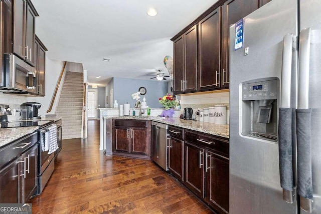 kitchen with dark wood-style flooring, light stone countertops, stainless steel appliances, dark brown cabinets, and backsplash