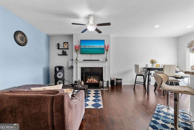 living room featuring recessed lighting, dark wood-style flooring, a ceiling fan, baseboards, and a glass covered fireplace