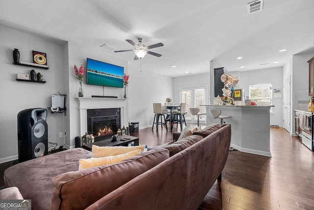 living room featuring baseboards, visible vents, a glass covered fireplace, dark wood-type flooring, and recessed lighting