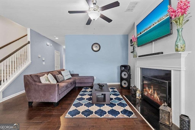 living area with visible vents, dark wood finished floors, baseboards, a fireplace with flush hearth, and stairs