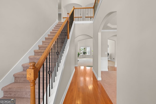 staircase featuring a high ceiling, ornamental molding, and hardwood / wood-style flooring