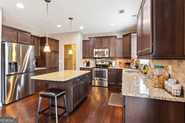 kitchen with pendant lighting, a kitchen breakfast bar, a center island, dark wood-type flooring, and appliances with stainless steel finishes