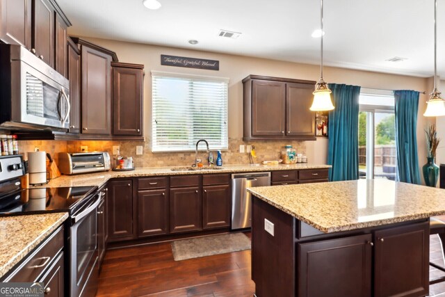 kitchen with a center island, decorative light fixtures, stainless steel appliances, and sink