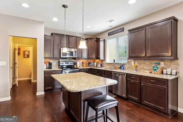 kitchen with pendant lighting, a kitchen island, stainless steel appliances, and dark hardwood / wood-style floors