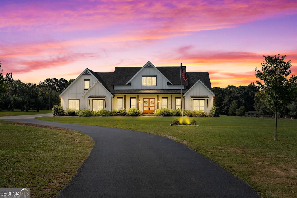 modern farmhouse style home with aphalt driveway, a lawn, board and batten siding, and roof with shingles