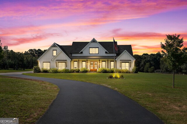 modern farmhouse style home with aphalt driveway, a lawn, board and batten siding, and roof with shingles