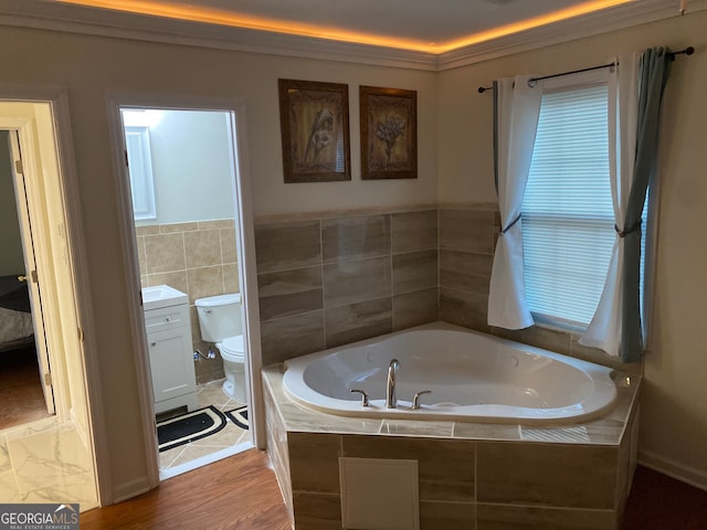 bathroom with hardwood / wood-style flooring, a relaxing tiled tub, toilet, and vanity