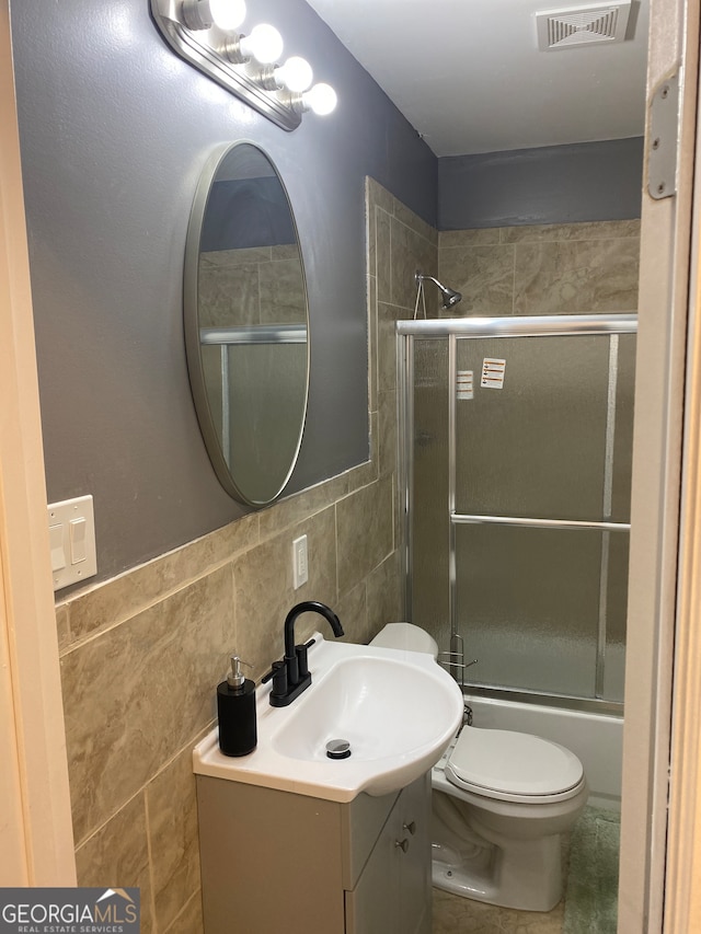 full bathroom featuring shower / bath combination with glass door, vanity, tile walls, and toilet