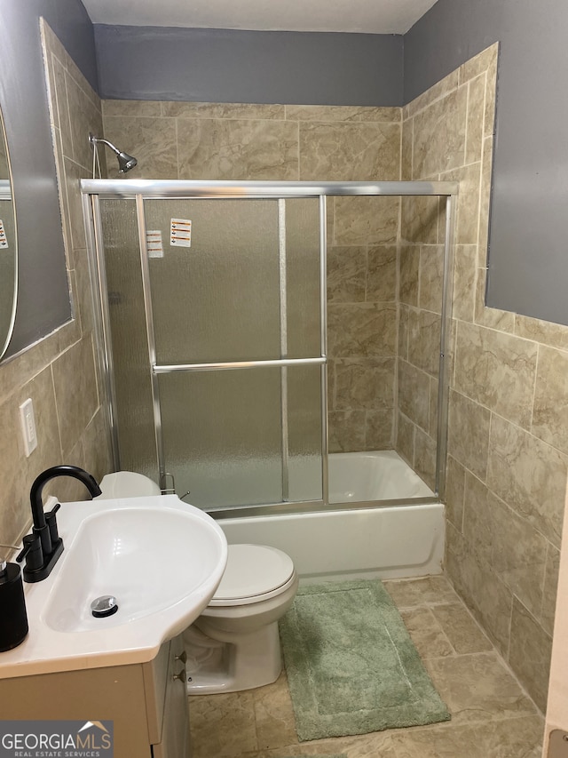 full bathroom with toilet, tile walls, vanity, and combined bath / shower with glass door