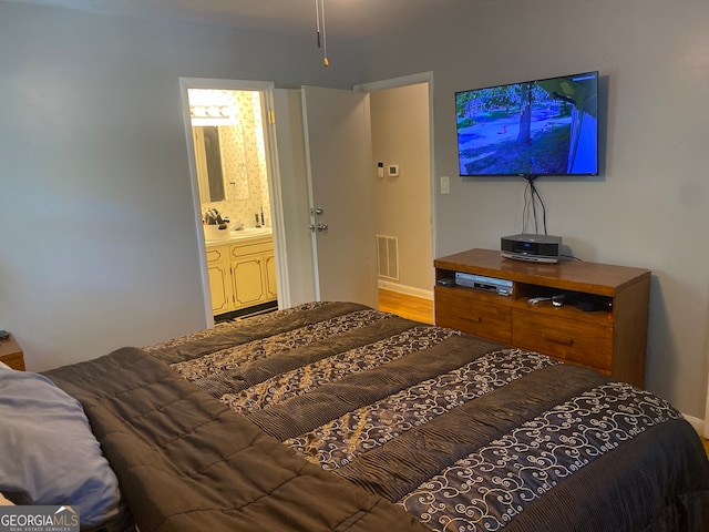 bedroom with ensuite bath and wood-type flooring