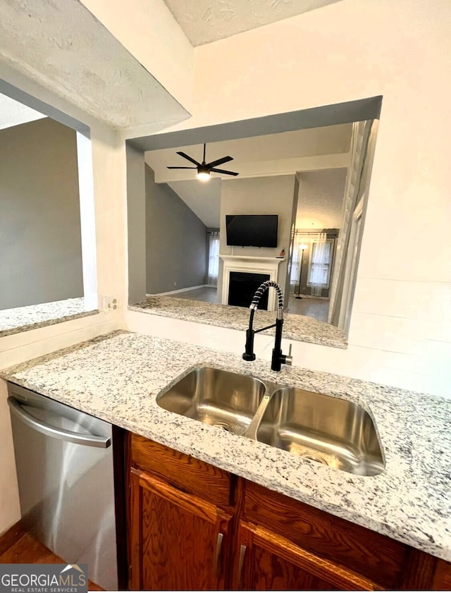 kitchen featuring ceiling fan, a fireplace, a sink, stainless steel dishwasher, and light stone countertops