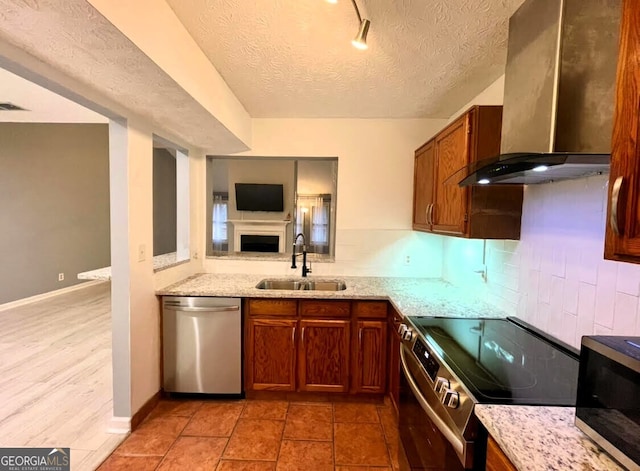 kitchen featuring light stone counters, a sink, open floor plan, appliances with stainless steel finishes, and wall chimney exhaust hood