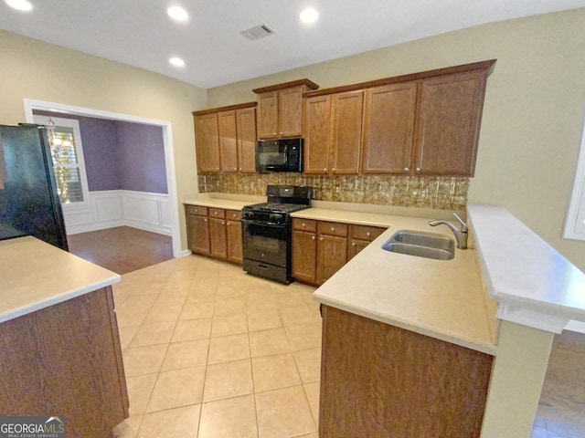 kitchen featuring brown cabinets, light countertops, a sink, a peninsula, and black appliances