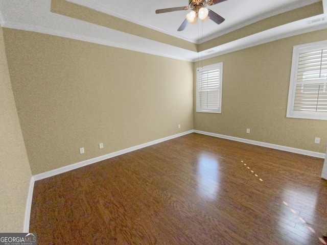 empty room featuring a tray ceiling, wood finished floors, visible vents, and baseboards