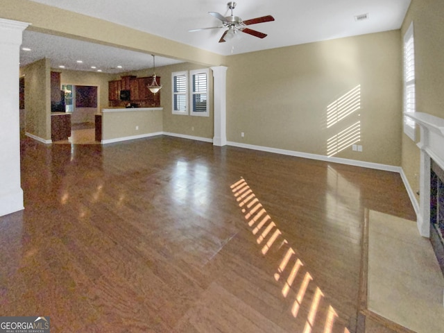 unfurnished living room with ceiling fan, dark wood-style flooring, a fireplace with flush hearth, baseboards, and decorative columns