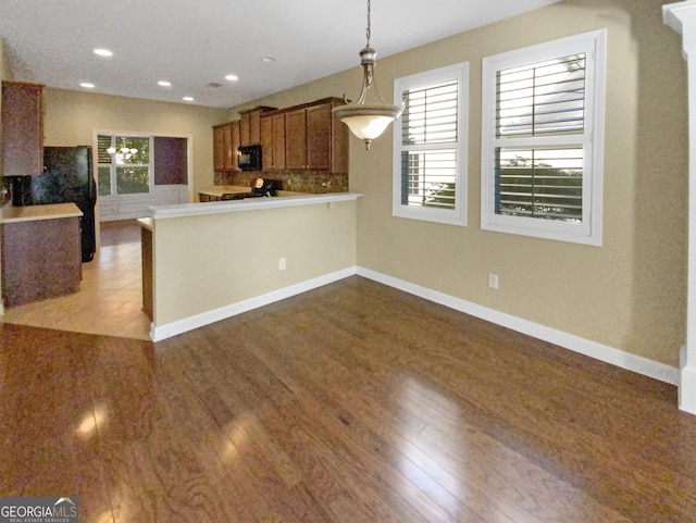 kitchen with light wood finished floors, brown cabinetry, a peninsula, black microwave, and pendant lighting