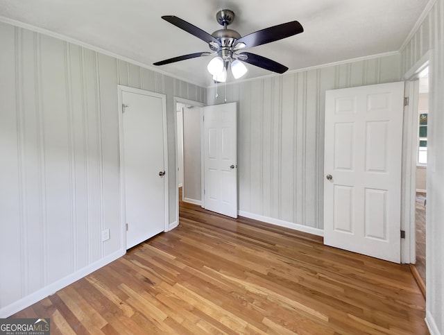 unfurnished bedroom featuring ceiling fan, crown molding, baseboards, and wood finished floors